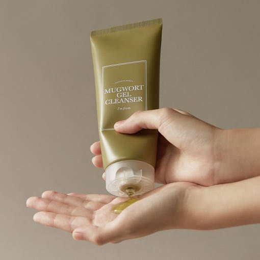 Green tube dispensing gentle mugwort gel cleanser onto open palm against neutral background