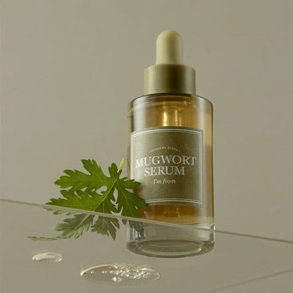 Clear glass dropper bottle of soothing mugwort serum with fresh green leaf and subtle liquid drops nearby