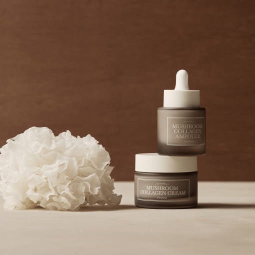 Brown frosted glass ampoule and cream containers with white lids paired with a textured white natural sponge on beige surface