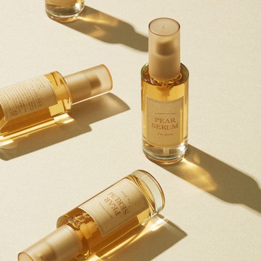 Glass bottles of pear serum with golden liquid and pump tops casting soft shadows on a light surface