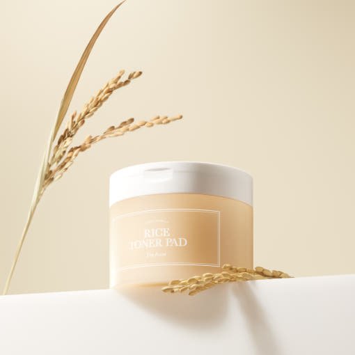 Round translucent container of toner pads with natural rice stalks on soft beige background with hydration focus