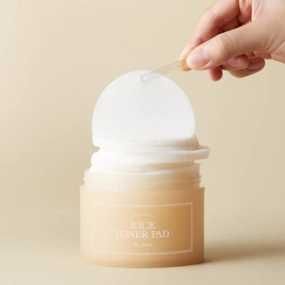 Hand removing a round toner pad from a beige container with a clear spatula on neutral background