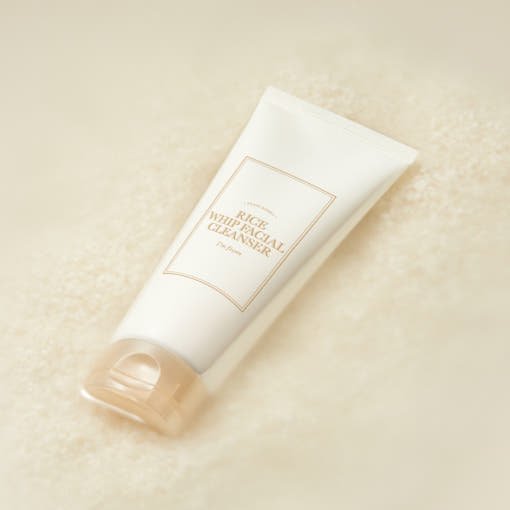 White tube of moisturizing facial cleanser with beige cap resting on soft textured rice grains background
