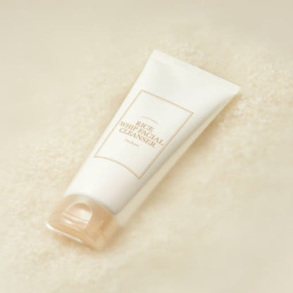 White tube of moisturizing facial cleanser with beige cap resting on soft textured rice grains background