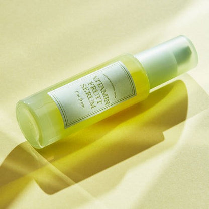 Frosted glass bottle of brightening vitamin fruit serum with soft yellow liquid and matte white cap on light background