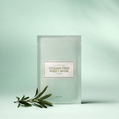 Matte light green packet of vitamin tree sheet mask with a fresh green plant sprig on a soft pale background