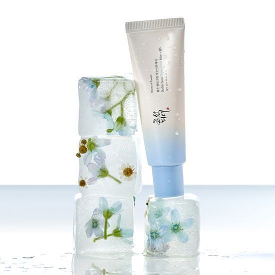 Tube of hydrating sun cream with pale blue cap resting on stacked ice cubes containing delicate flowers inside