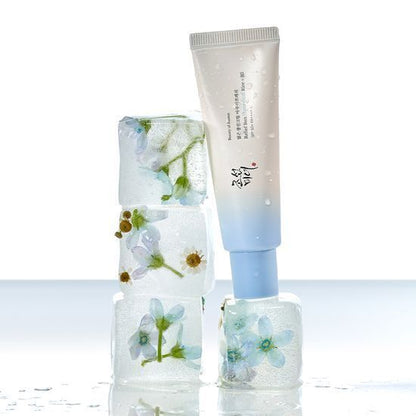 Tube of hydrating sun cream with pale blue cap resting on stacked ice cubes containing delicate flowers inside