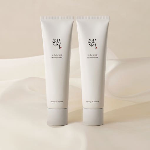 Two minimalist white tubes of hydrating cream with subtle black and red text on soft beige fabric background