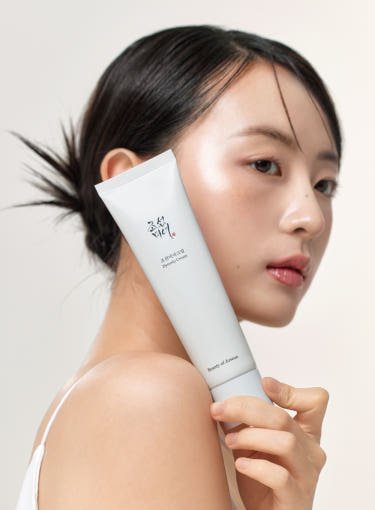 Minimalist white tube of hydrating cream held by woman with glowing, dewy skin against a soft beige background