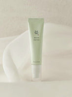 Pale green tube of brightening serum with simple black Korean text standing on soft white fabric background