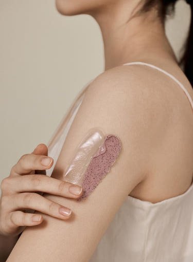Close-up of a woman applying smooth and textured skincare mask swatches on her upper arm for deep cleansing benefits