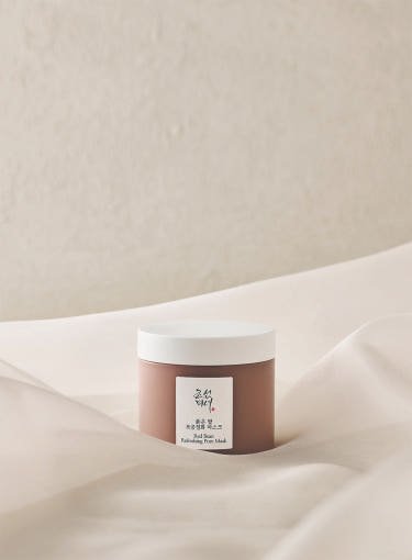 Matte brown jar with white lid of pore-cleansing mask set against soft beige fabric background
