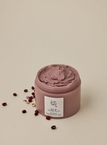 Open jar of smooth textured pore-cleansing mask with natural red beans scattered on beige surface