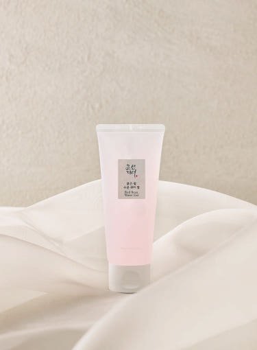 Soft pink tube of hydrating water gel with minimalistic label placed on flowing cream fabric background