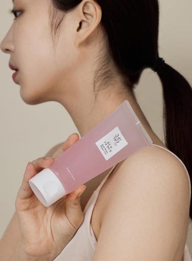 Woman holding a pink tube of hydrating water gel against her shoulder with natural skin and sleek ponytail hairstyle