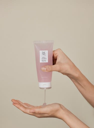 Person dispensing light pink gel from soft tube onto open palm against neutral background