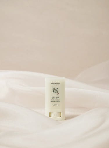 Minimalist matte sun stick with soft green packaging placed on sheer white fabric background