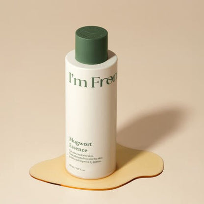 Tall white bottle with green cap of hydrating Mugwort Essence on beige surface with liquid spill shadow