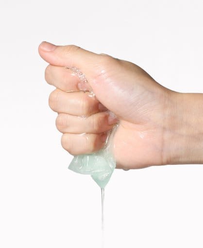 Hand squeezing a translucent hydrating serum gel with a thin strand dripping downward