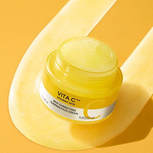 Open jar of yellow brightening sleeping mask cream with visible gel texture on matching yellow background