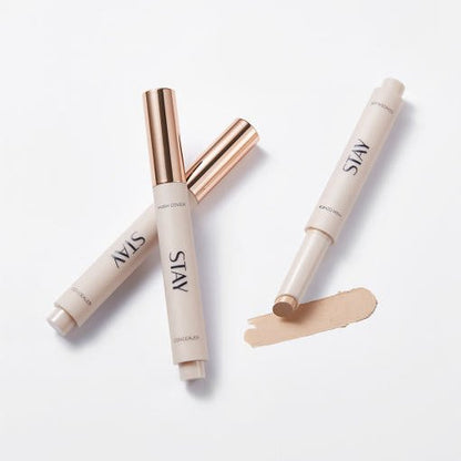 Beige concealer sticks with metallic rose gold caps and creamy high coverage formula swatch on white background