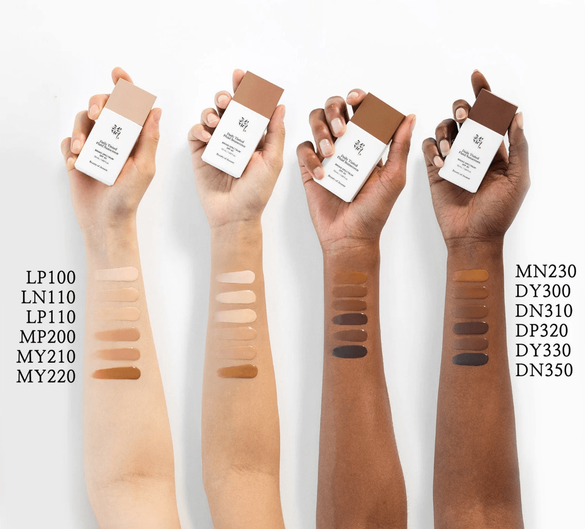 Four arms with different skin tones showing swatches of tinted fluid sunscreen shades alongside matching product bottles above each arm