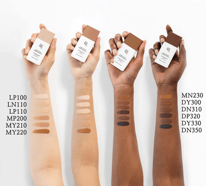 Four arms with different skin tones showing swatches of tinted fluid sunscreen shades alongside matching product bottles above each arm