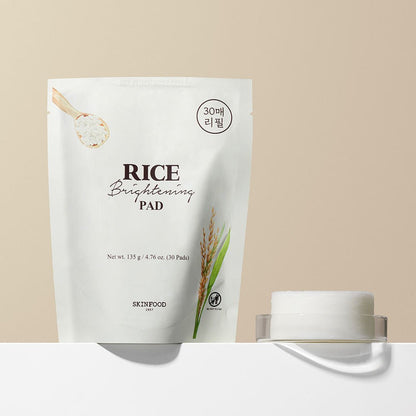 White refill pack of brightening rice skincare pads beside closed transparent container on beige surface