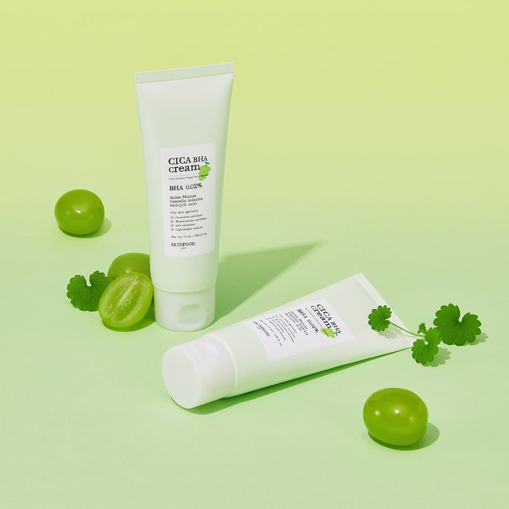 Two tubes of soothing cream with smooth texture beside fresh muscat grapes and green leaves on light background