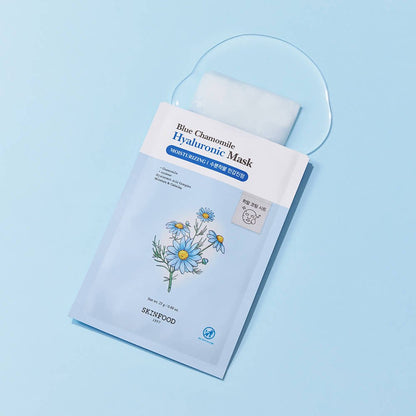 Light blue packet of hydrating facial sheet mask with chamomile flower illustration on blue surface with serum spilled
