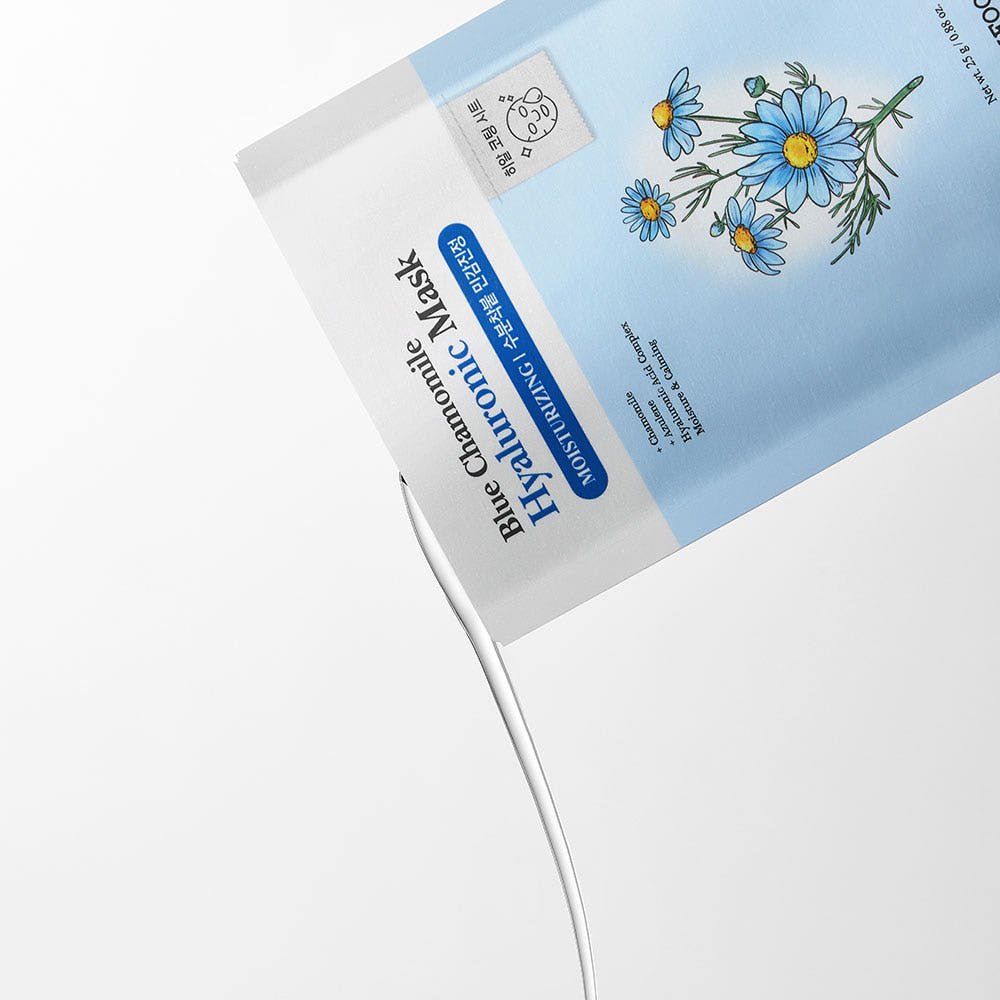 Close-up of blue chamomile mask packaging with creamy white serum flowing out against white background