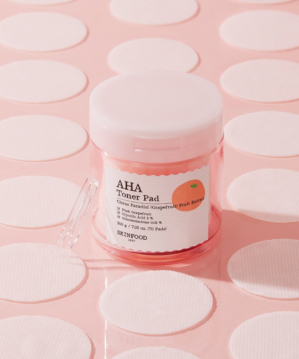 Clear container of pink grapefruit toner pads surrounded by round exfoliating pads on soft pink surface