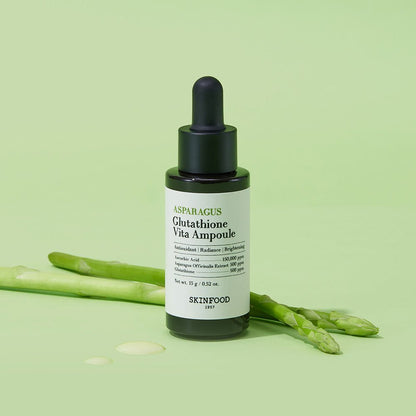 Dark glass dropper bottle of brightening ampoule with fresh asparagus stalks and serum drops on light green surface