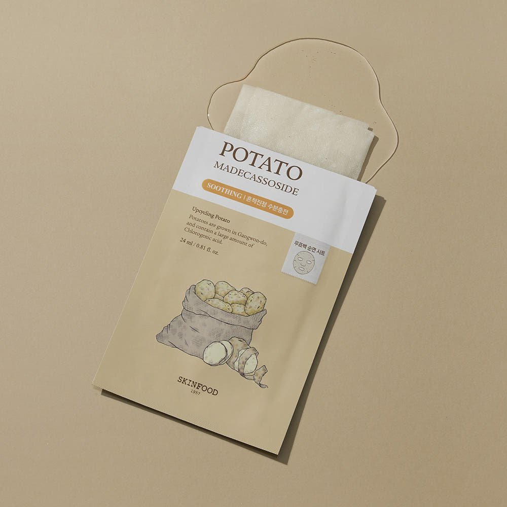 Beige sheet mask partially pulled out of a soothing potato-infused skincare packet on neutral background