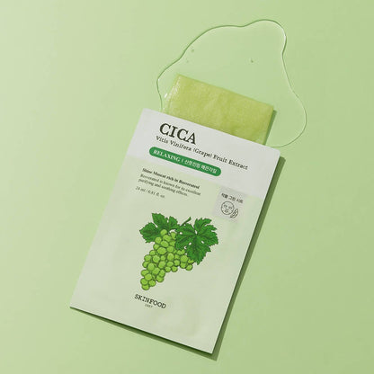 Light green sheet mask partially pulled out of white sachet featuring grape illustration and clear serum spill on pale green surface