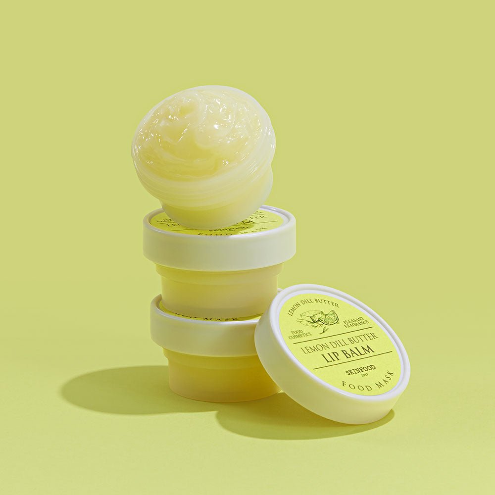 Stack of creamy lemon dill butter lip balm jars with one open showing smooth pale yellow balm texture