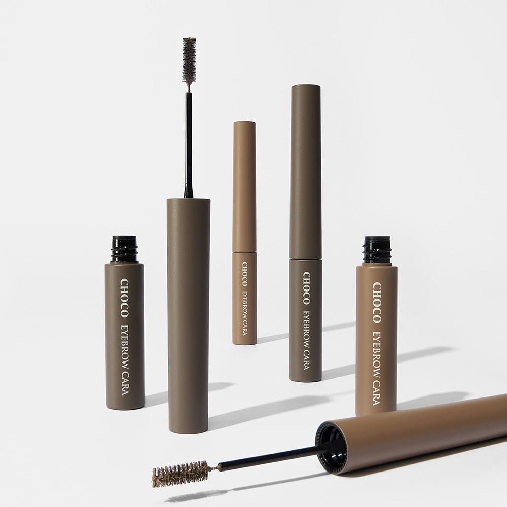Multiple neutral brown eyebrow mascara tubes with brush wands for defined brows on white background