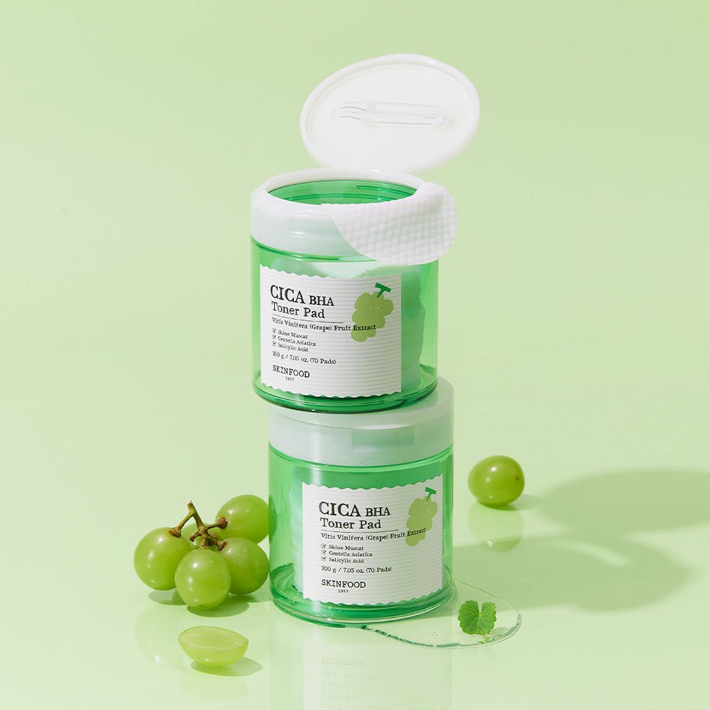 Two green toner pad jars stacked on pale green background with fresh Shine Muscat grapes and leaves nearby