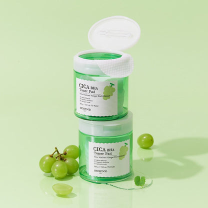 Two green toner pad jars stacked on pale green background with fresh Shine Muscat grapes and leaves nearby