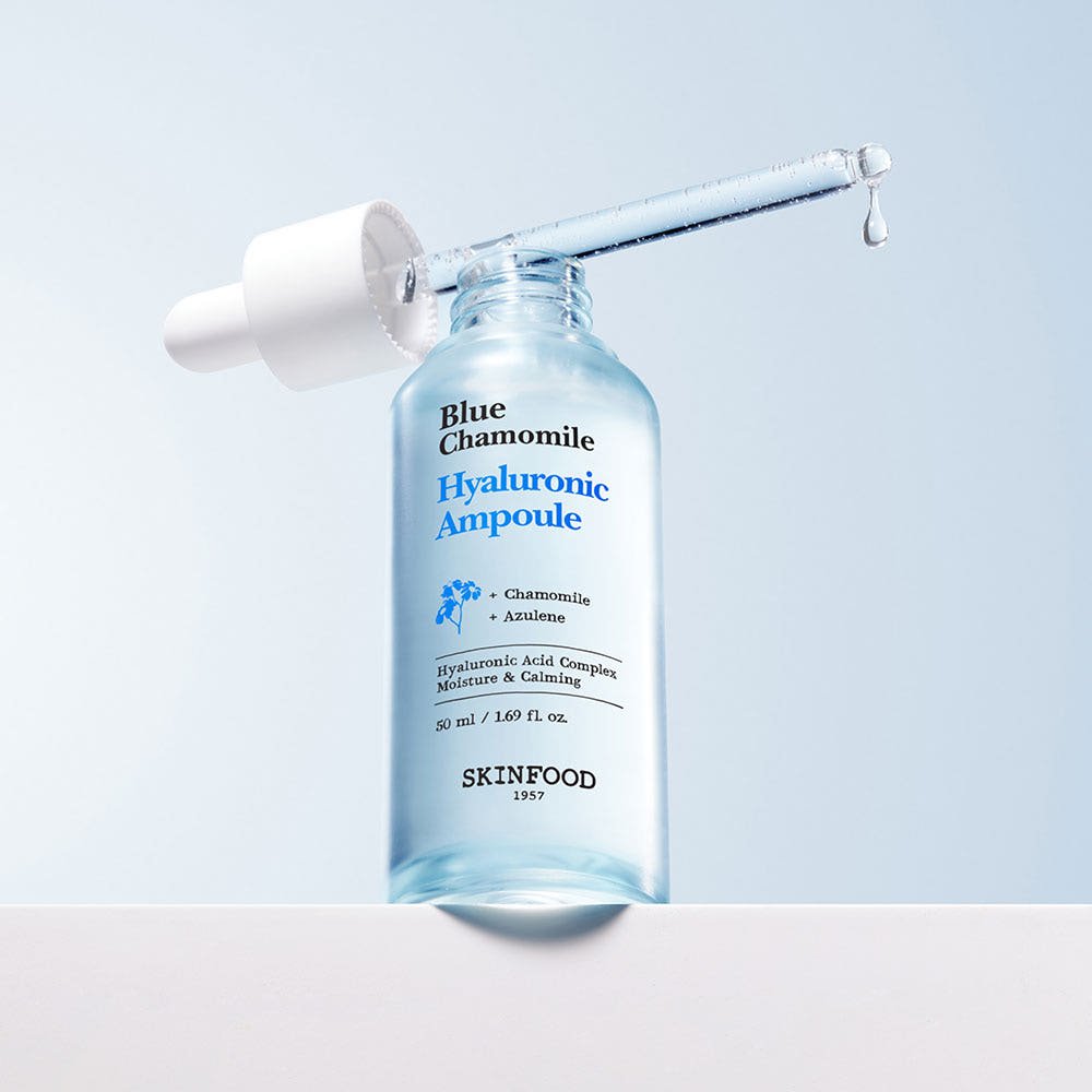 Blue chamomile hyaluronic ampoule bottle with dropper releasing clear serum drop against soft blue background