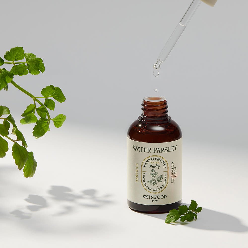 Amber glass dropper bottle with water parsley extract ampoule and fresh parsley leaves on white surface