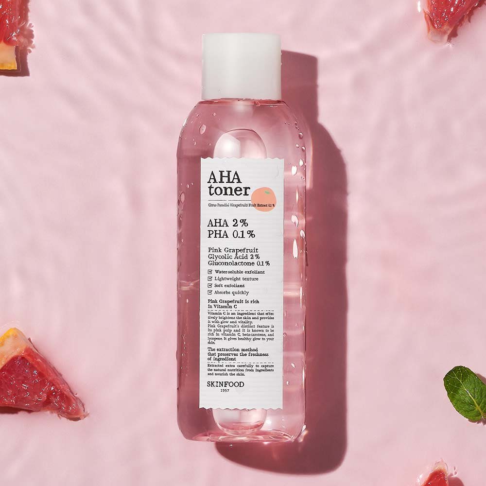 Clear pink toner bottle with white label highlighting exfoliating acids on a soft pink background with grapefruit pieces