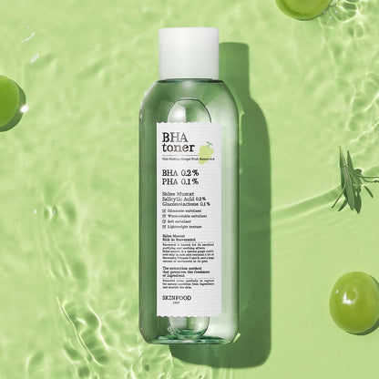 Clear green toner bottle with white label surrounded by Shine Muscat grapes and leaves on textured green surface