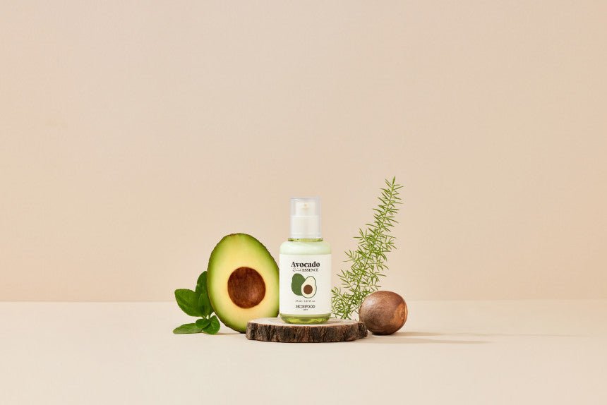 Small white bottle of avocado essence with green leaves and half an avocado on beige background