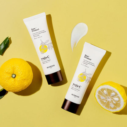 Two tubes of brightening yellow citrus tone-up cream with sun protection beside fresh whole and cut yuja fruit on yellow background