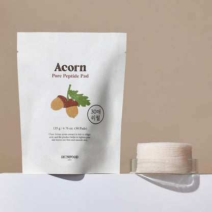 White pouch of pore tightening peptide pads with acorn illustration beside a stack of round cotton pads on clear holder