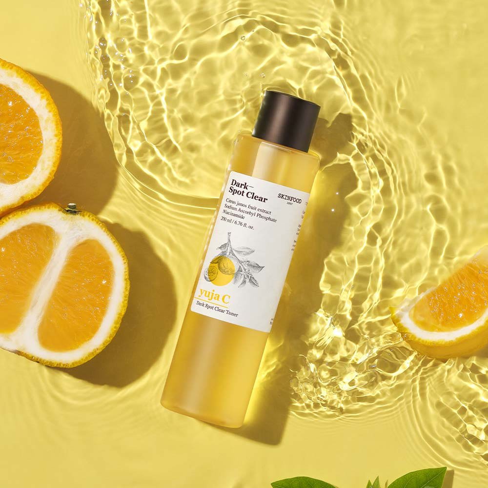 Clear toner bottle with citrus fruit slices on yellow background highlighting brightening benefits