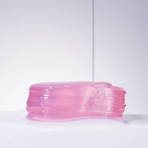 Glossy pink hydrogel eye patch with smooth, gel-like texture and clear liquid dripping on a white surface