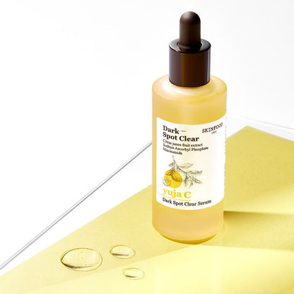 Frosted glass dropper bottle of brightening yuja C dark spot serum on yellow paper with serum droplets nearby